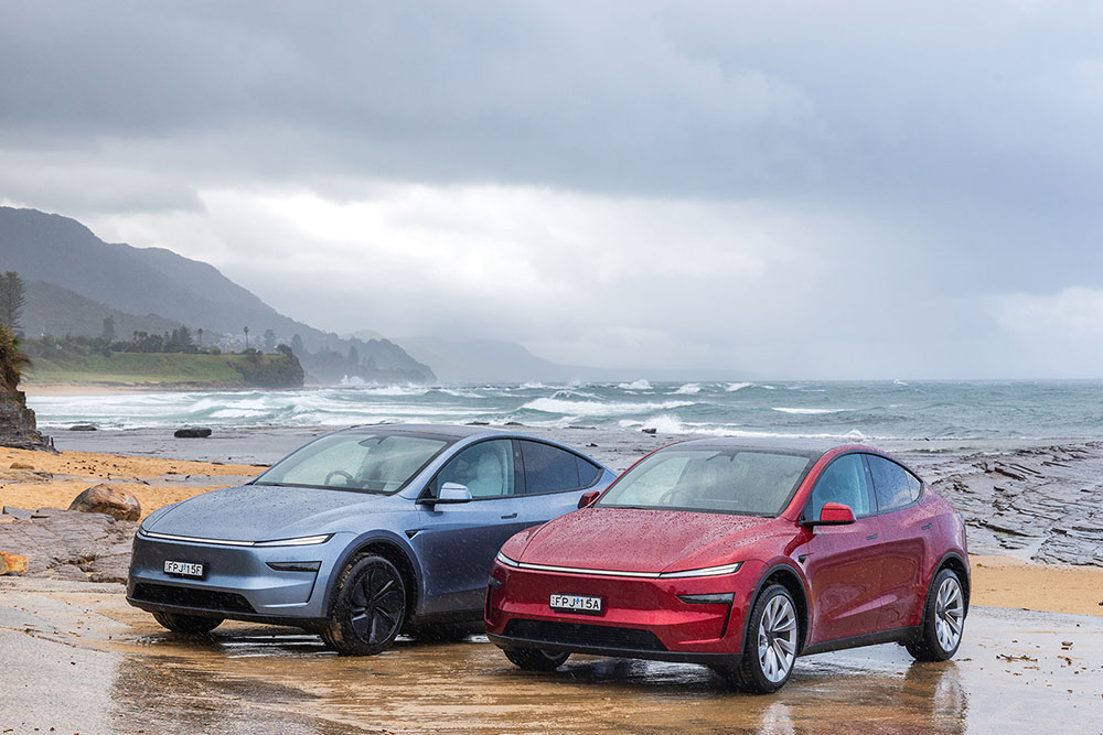 Two 2025 Tesla Model Y cars parked on the beach.